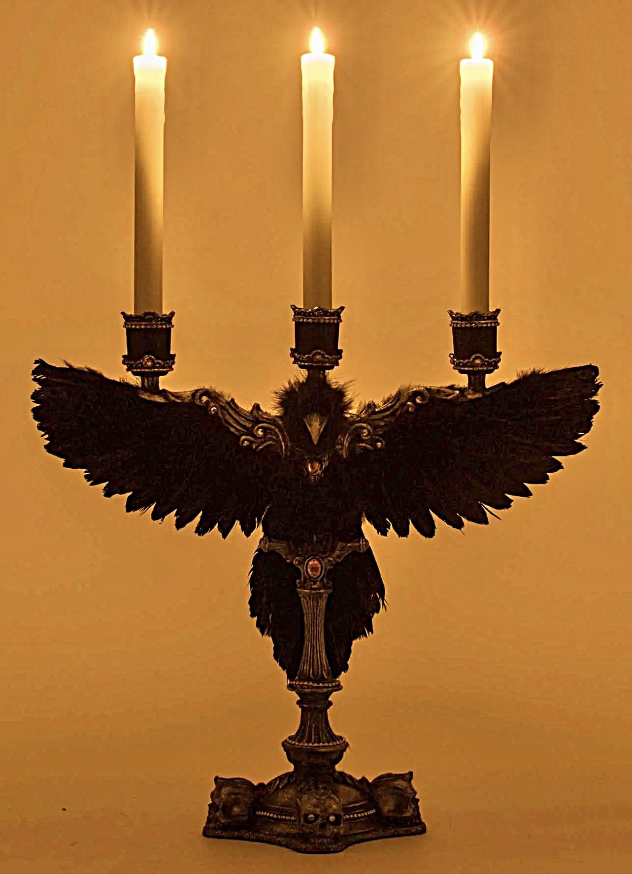 Decorative candle holder with feathers and three lit candles on a plain background