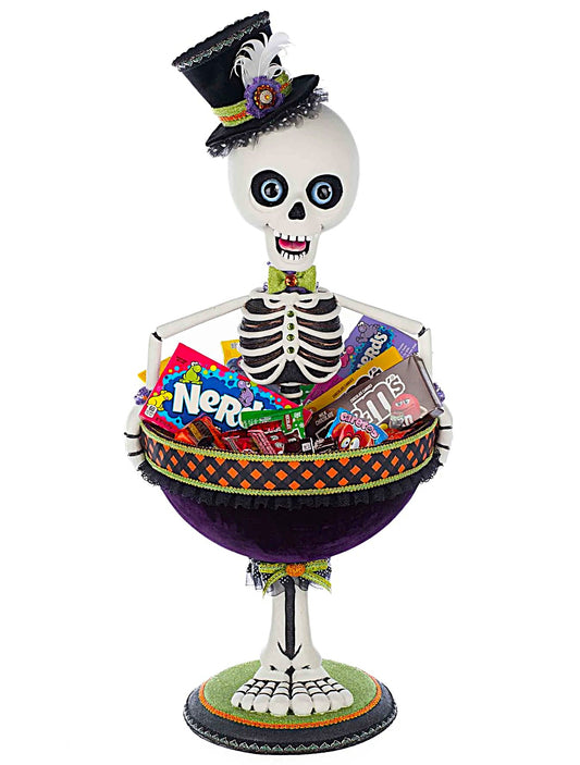 Skeleton figure with a top hat holding a bowl of Halloween candy on a white background
