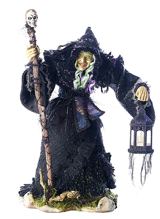 Decorative witch figurine holding a lantern and staff on a white background
