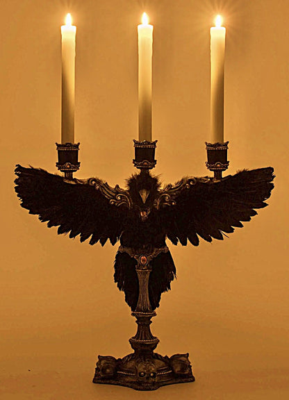 Decorative candle holder with feathers and three lit candles on a plain background